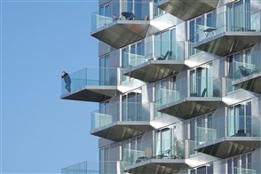 Bewoner kijkt vanaf balkon appartementengebouw..