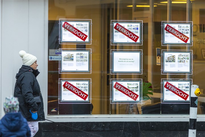 A pedestrian walks past a real estate agent with signs in the window advertising properties for sale and sold.